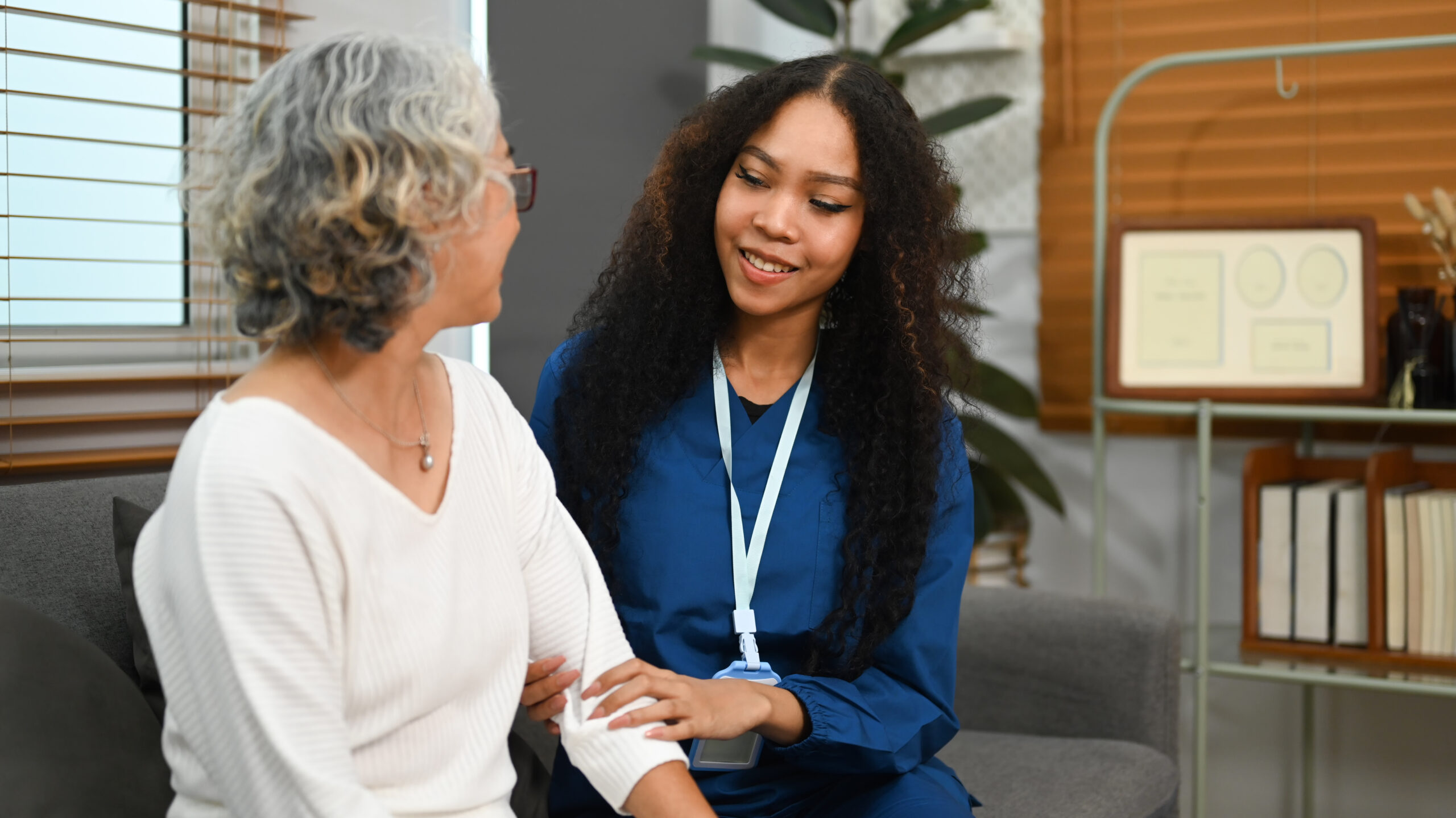 Caregiver assists an elderly woman on a couch